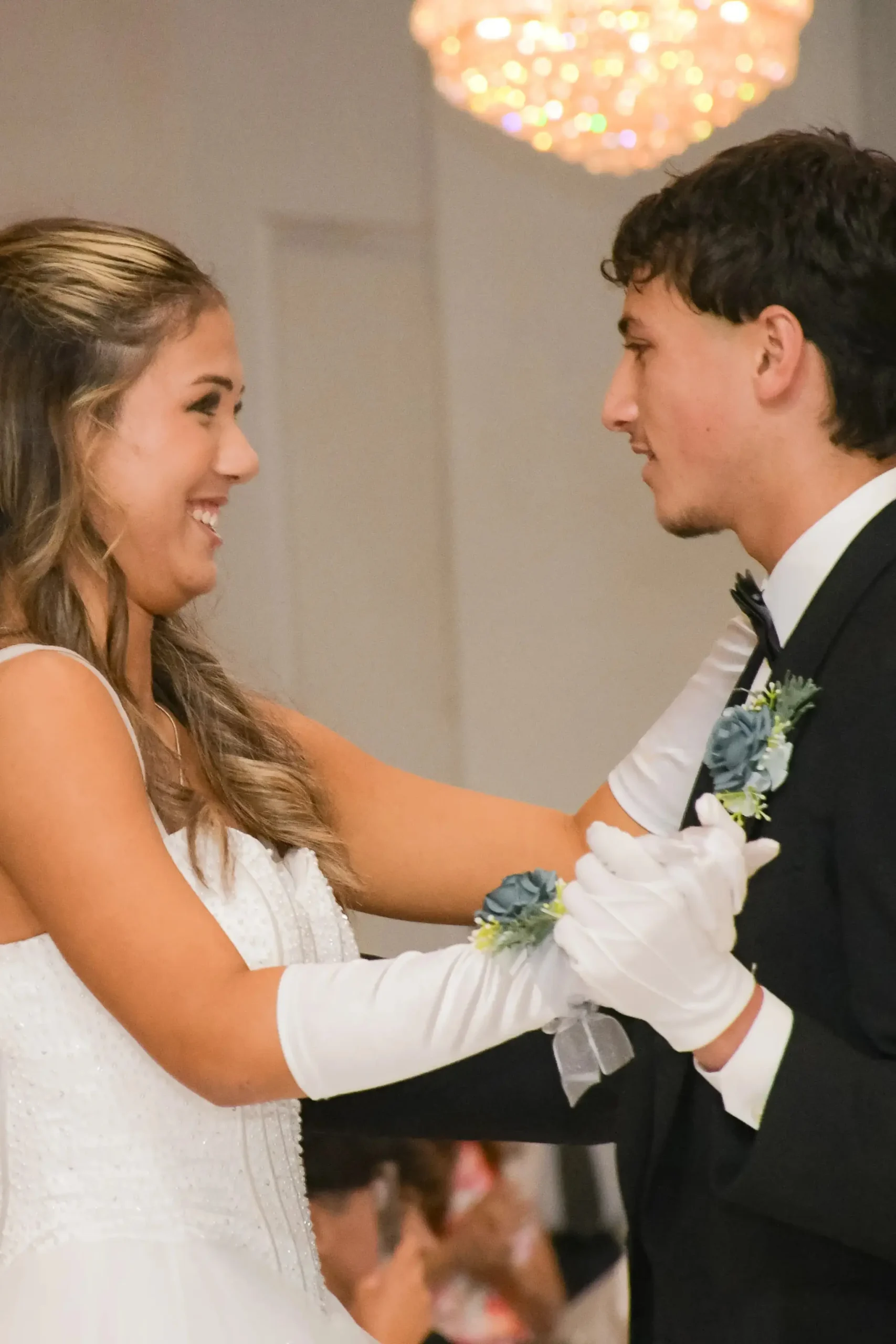 A smiling couple in formal debutante attire dancing and looking at each other.