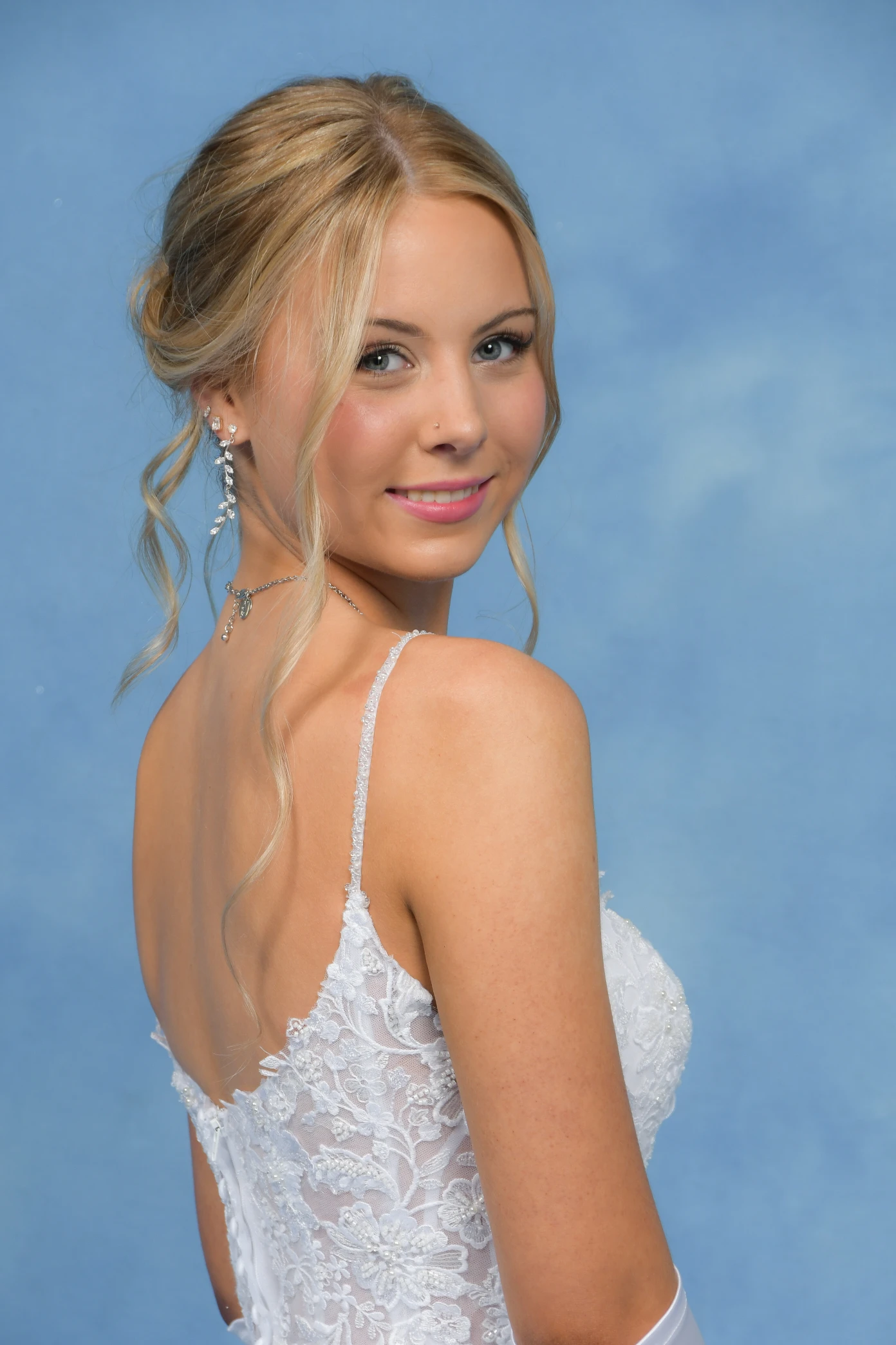 Debutante in a white lace gown with an updo hairstyle, posing against a blue background.